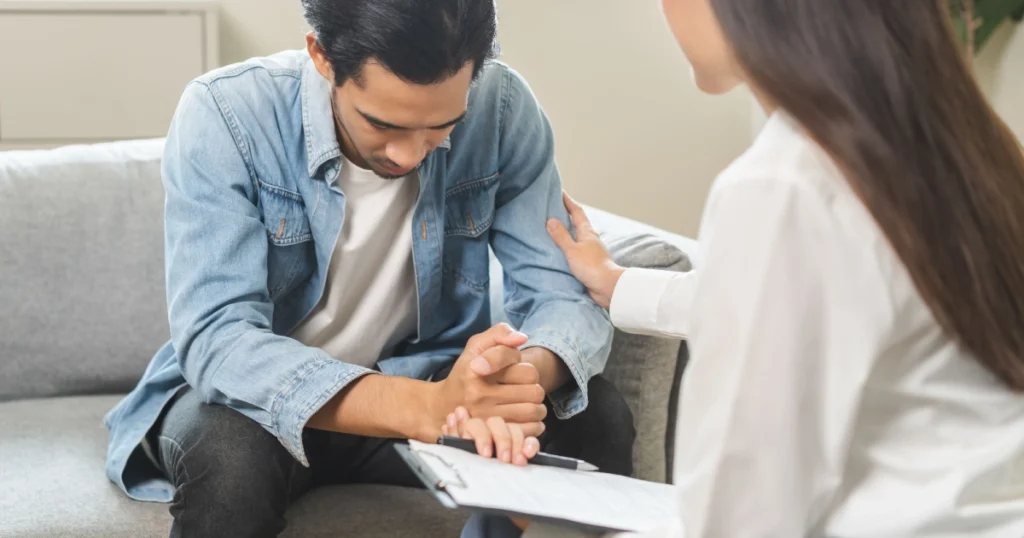 Woman comforting a sad man with a hand on his shoulder while holding a clipboard during Ketamine Infusion Therapy in Buford, GA.